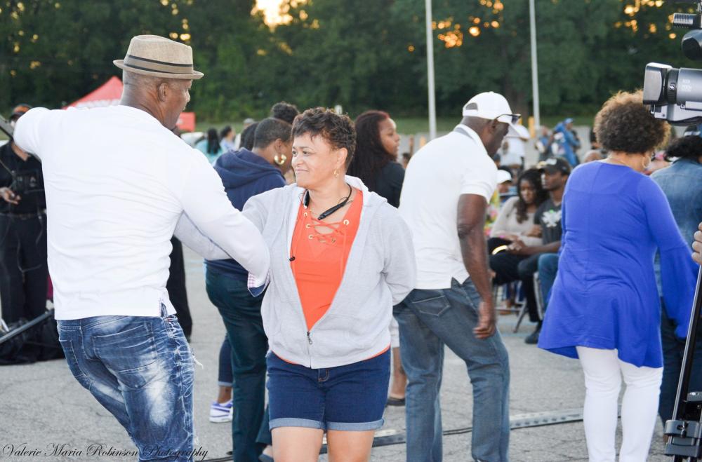 Couple dances together in a parking lot, surrounded by other dancing individuals
