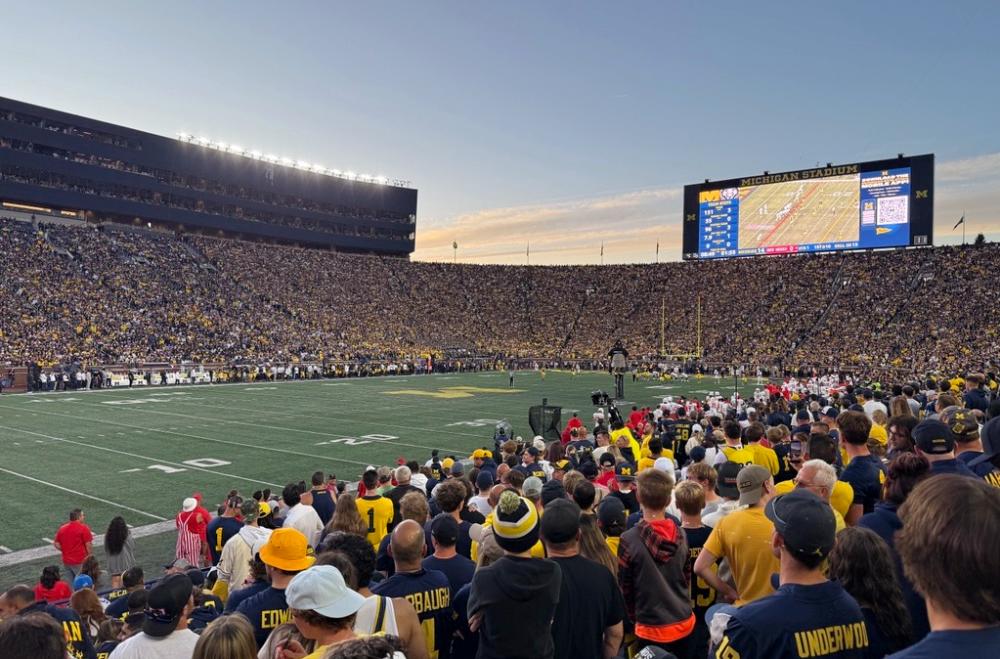 A football game is being played on green turf with spectators filling the stadium. The jumbotron is lit up and stands tall above the stadium.