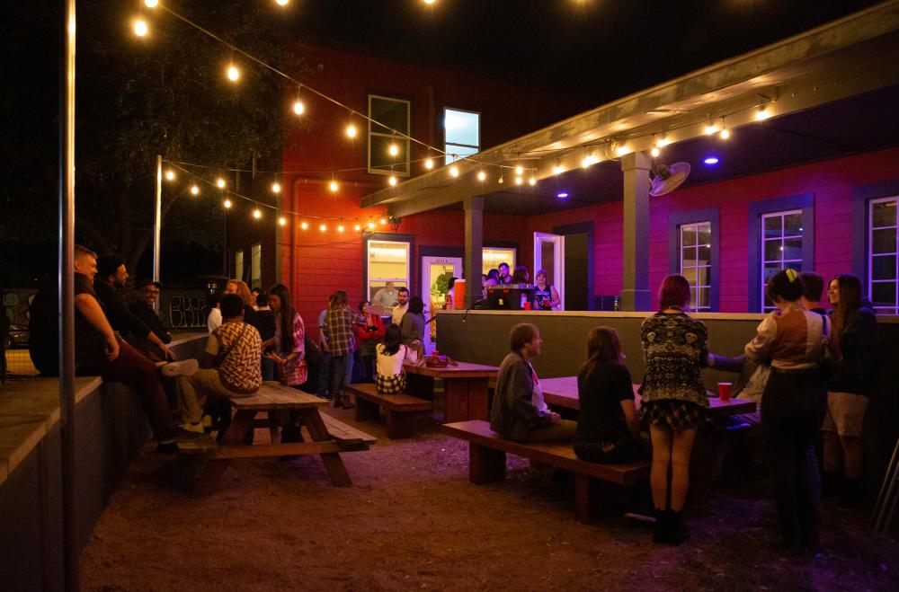 The patio at ColdTowne Theater illuminated at night by yellow string lights with people sitting at patio tables chatting.