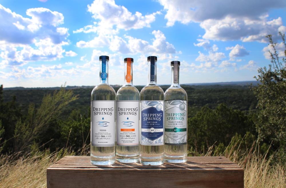 Four bottles of Dripping Springs Vodka and gin in front of hill country landscape