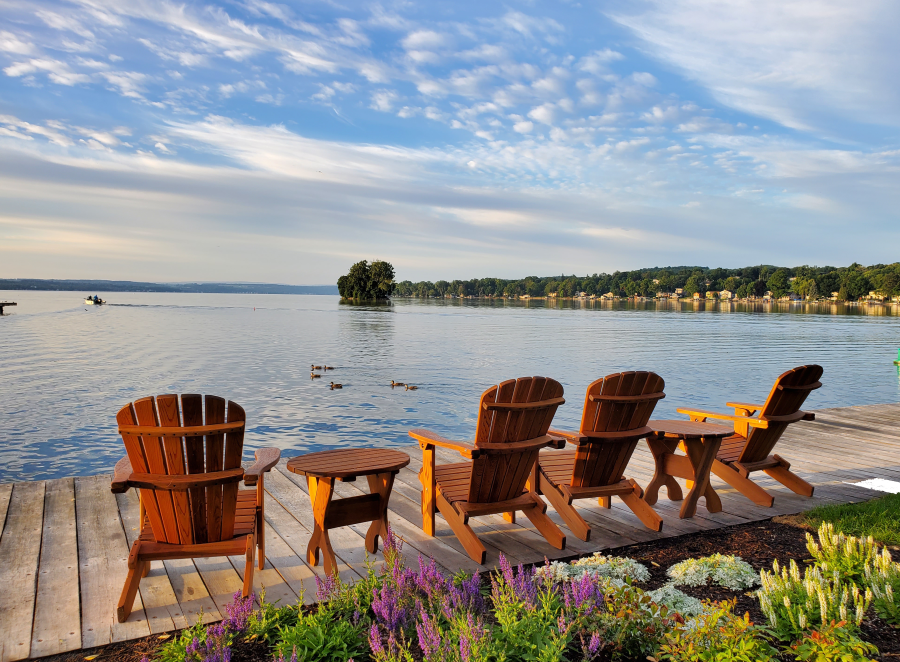 Adirondack chairs on a dock over looking Canandaigua Lake on a sunny day. Skenoh Island can be seen in the distance.