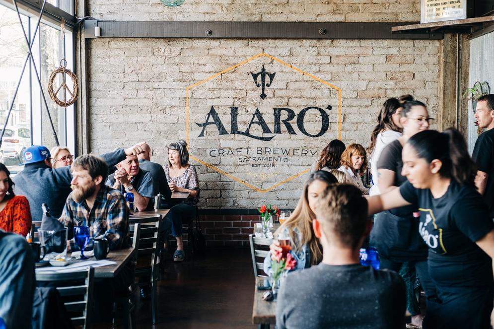 people eating inside a restaurant that has alaro craft brewery painted on the back brick wall