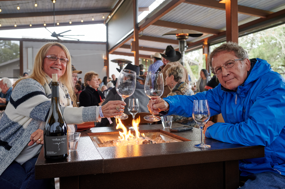 Couple clinking glasses of William Chris wine over an open firepit during New Year's Black-Eyed Pea Cook-Off event.