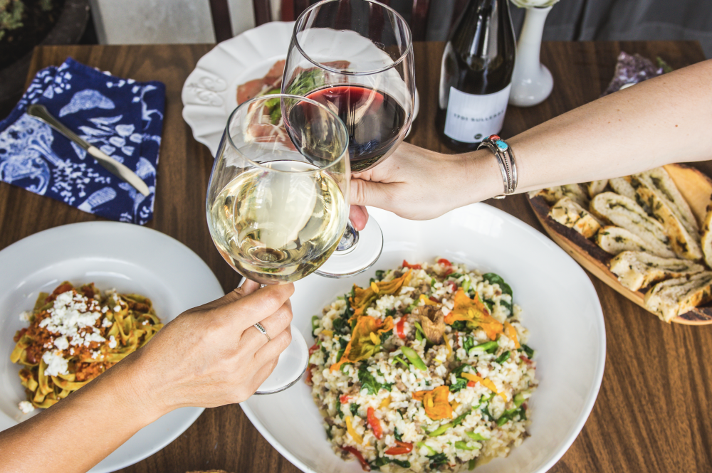 clinking two glasses of wine over table with three dishes at Andiamo Ristorante in Austin Texas