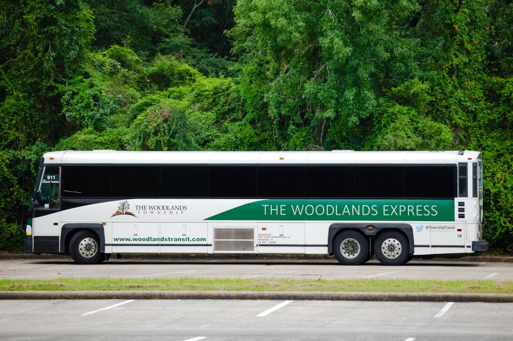 The Woodlands Express (aka Rodeo Shuttle) is a white city bus branded with "The Woodlands Township" and " THE WOODLANDS EXPRESS" along the side.