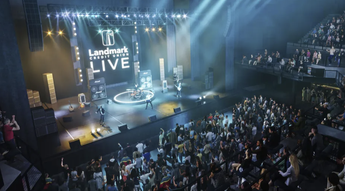 Wide view of a live concert inside Landmark Credit Union Live, with a band performing on a brightly lit stage and a large crowd gathered on the main floor and balcony seating.