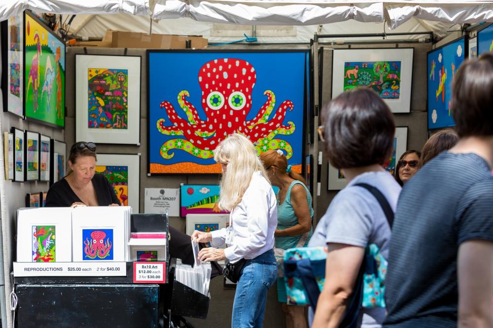 several people browse inside an artist's vendor booth during a festival.