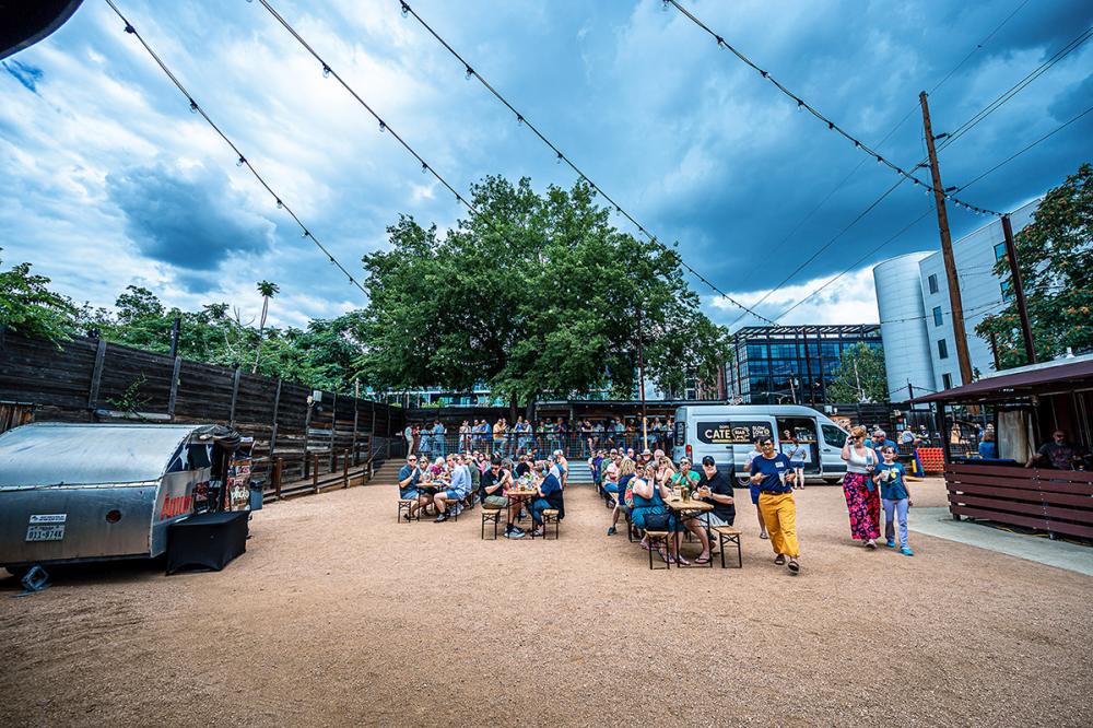 People sitting at picnic tables in a backyard-music venue setting.
