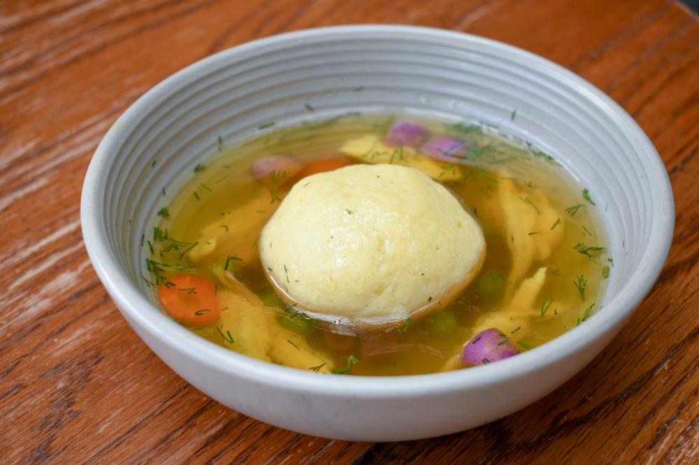 A close-up image of matzo ball soup sitting on a wooden table.