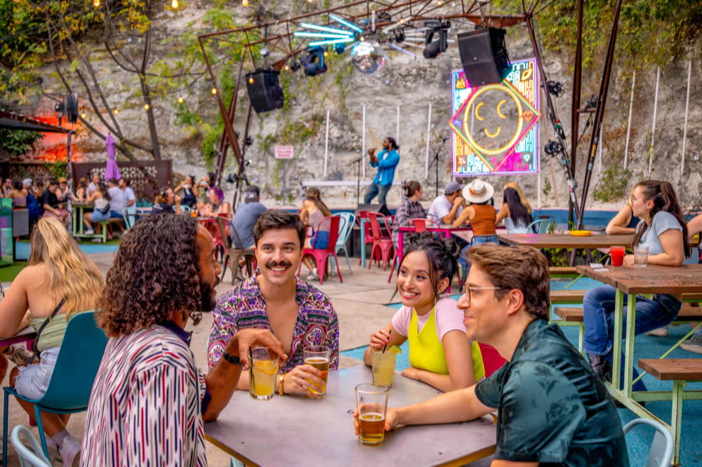 Image of a group of men and women sitting at table chatting with band onstage in the background at Cheer Up Charlies.