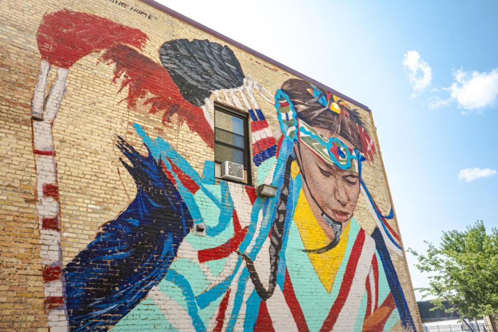 Coming Home mural of Native American women on the side of a tan brick building.