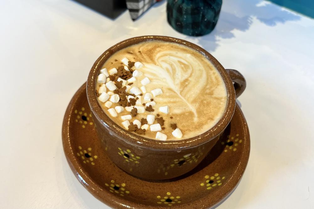 brown coffee mug filled with a latte and topped with mini marshmallows and tiny gingerbread men cookies