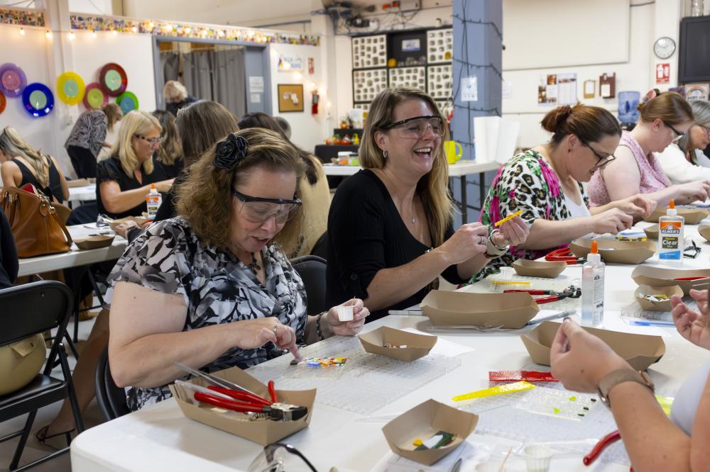 A group of women varying in age place glass pieces on a panel to create their very own kiln-fused creation at Glass Art Kalamazoo.