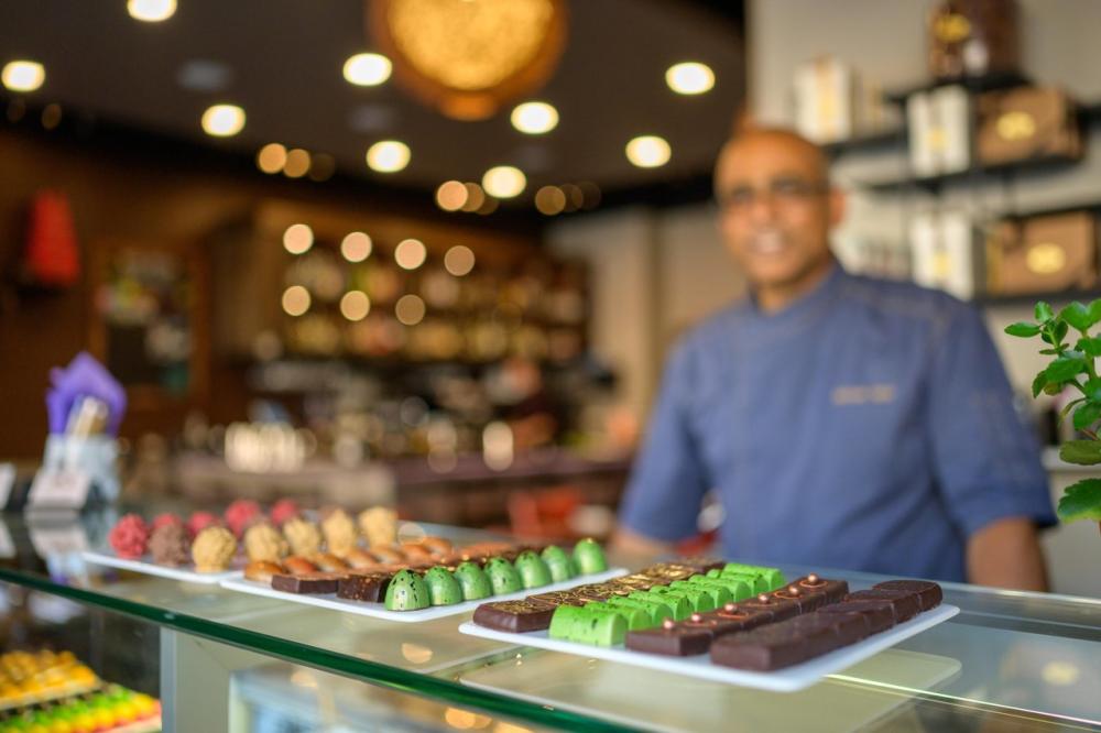 Chef Santosh Tiptur at The Conche in Loudoun County stands behind a glass display case filled with handcrafted chocolate truffles for wine pairing at Bluemont Vineyard