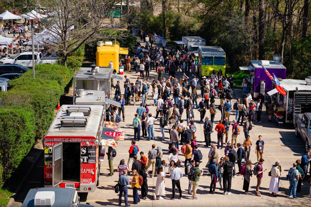 An overhead view of the Food Truck Village at LPSC. There are at least 10 food trucks along either side of a parking lot, each with long lines of customers from the convention. In the back, on the left, is another lot with white pop-up tents and tables for guests to eat their lunch.