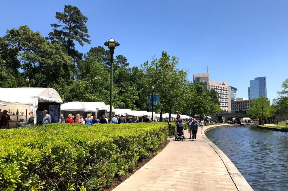 White tents line The Woodlands Waterway for The Woodlands Waterway Arts Festival. The viewer faces The Woodlands Waterway Marriott Hotel & Convention Center.