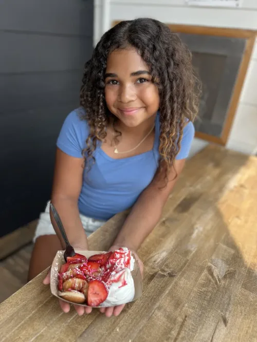 Young black girl holding a paper basket of strawberries and whipped cream