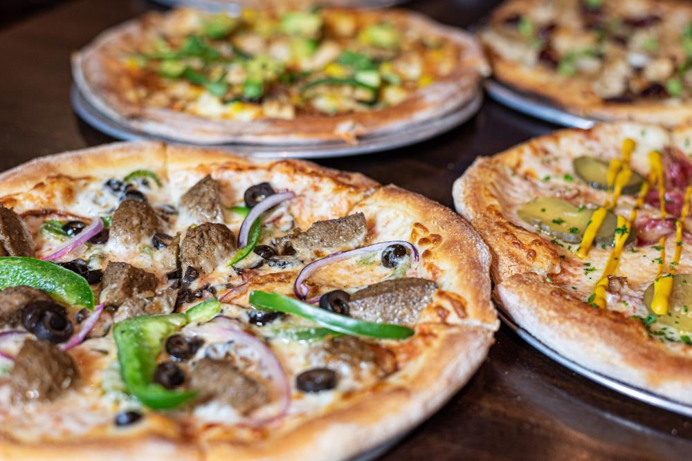 Image of four pizzas laid side-by-side on a wooden table.