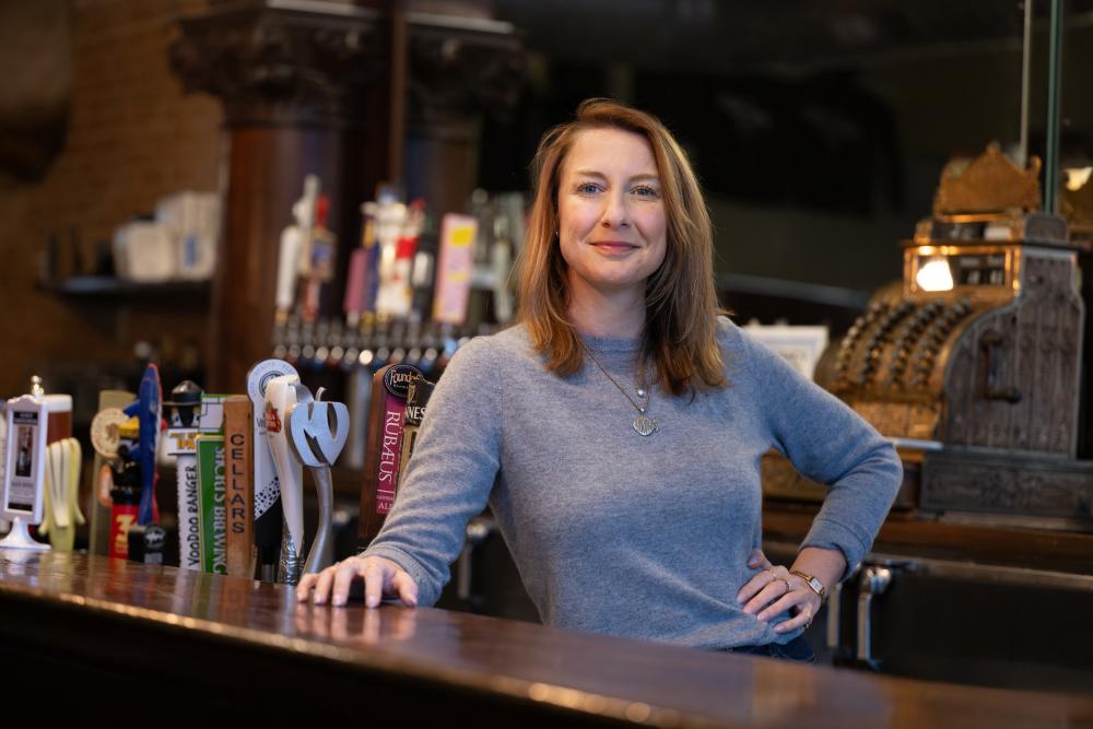 Woman stands behind a bar in a dimly-lit area  