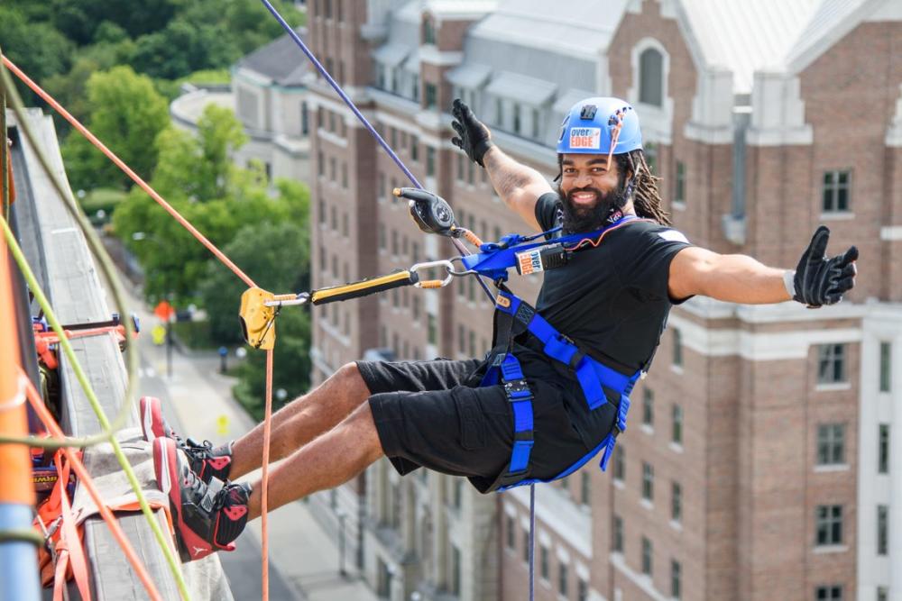 Man poses as he rappels off a tall building in a downtown area.