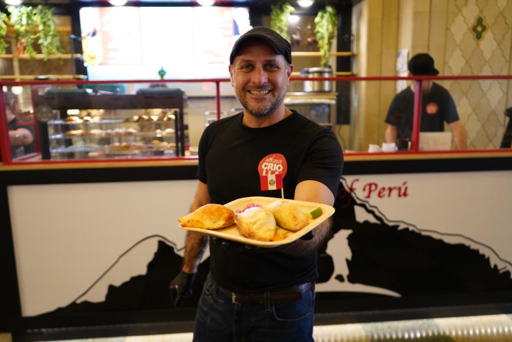 Man is standing holding plate of empanadas in front of restaurant Mikasa Criolla