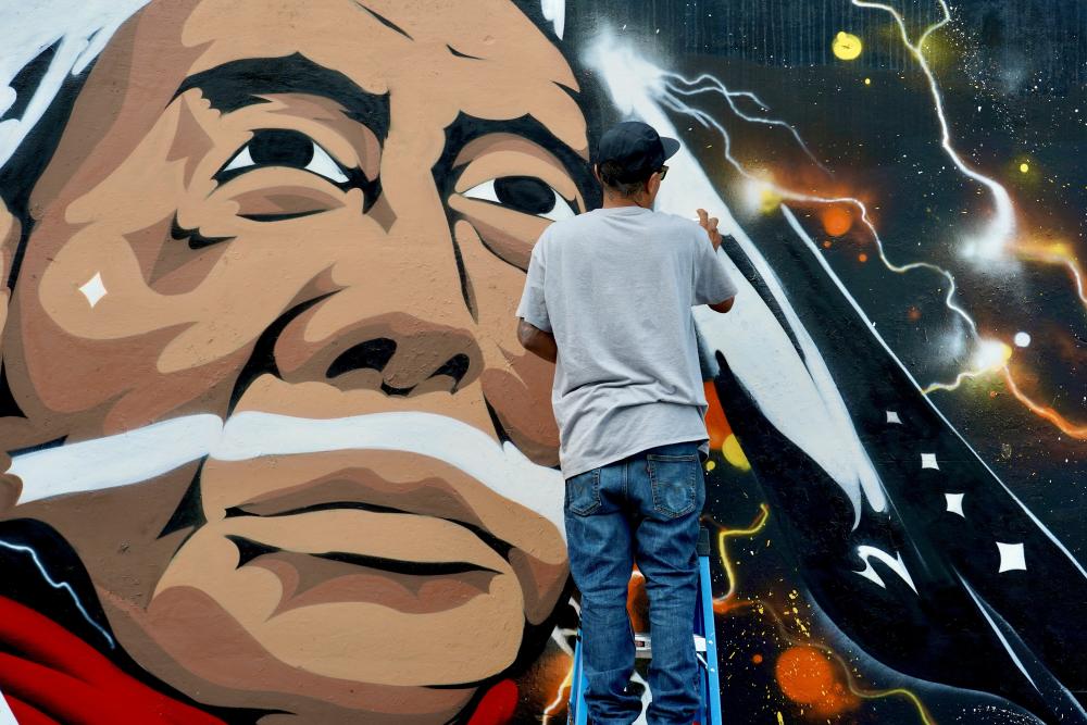 Man standing on a ladder using spray paint to create mural of Native American