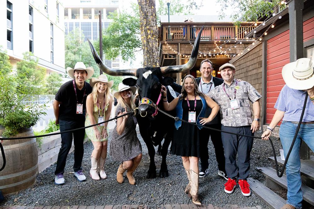 Group of people wearing cowboy hats and smiling at the camera while standing with a Longhorn.