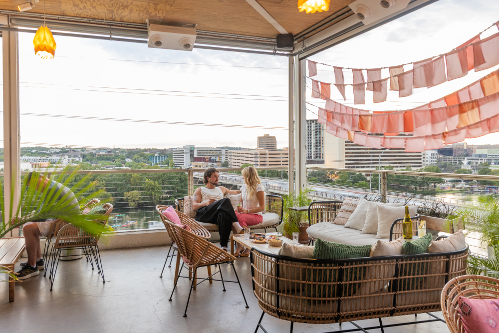 Two people sitting and talking the rooftop restaurant P6 at The LINE Hotel with Lady Bird Lake in the background.