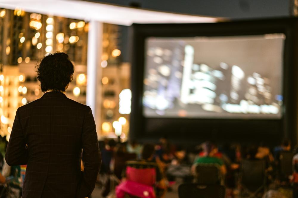 Back of man standing, watching towards a crowd and large film screen at Asian American Film Festival.