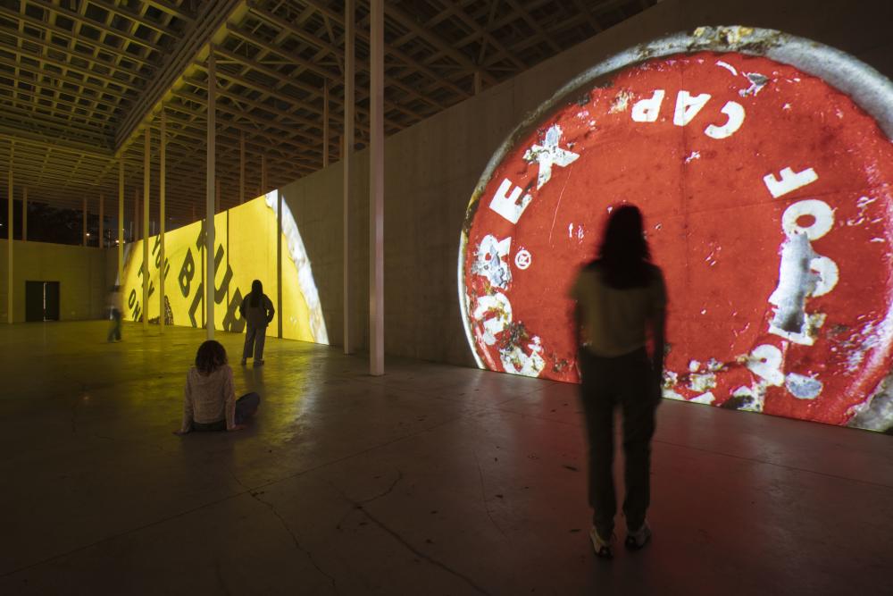 People standing in front of digital mural of red and yellow bottle caps.