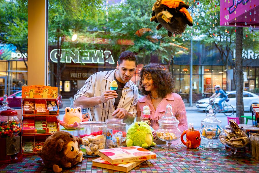 Couple window shopping at a toy store while holding ice cream cones.