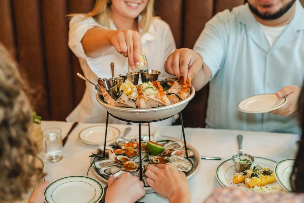 Photo shows four people reaching towards a seafood tower with various seafood items on ice