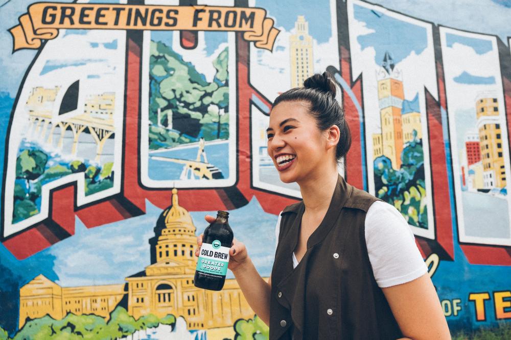 woman with bottled cold brew in front of Austin mural