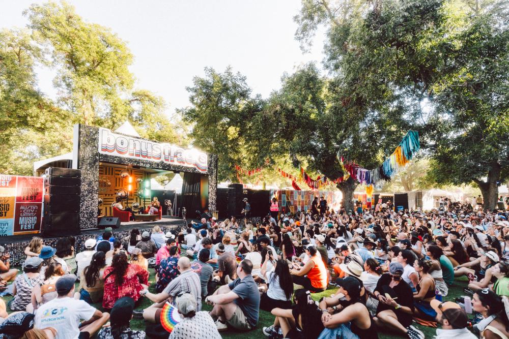 ACL Festival goers sitting on the grass and watching an artist interview on the Bonus Tracks stage at ACL Festival.