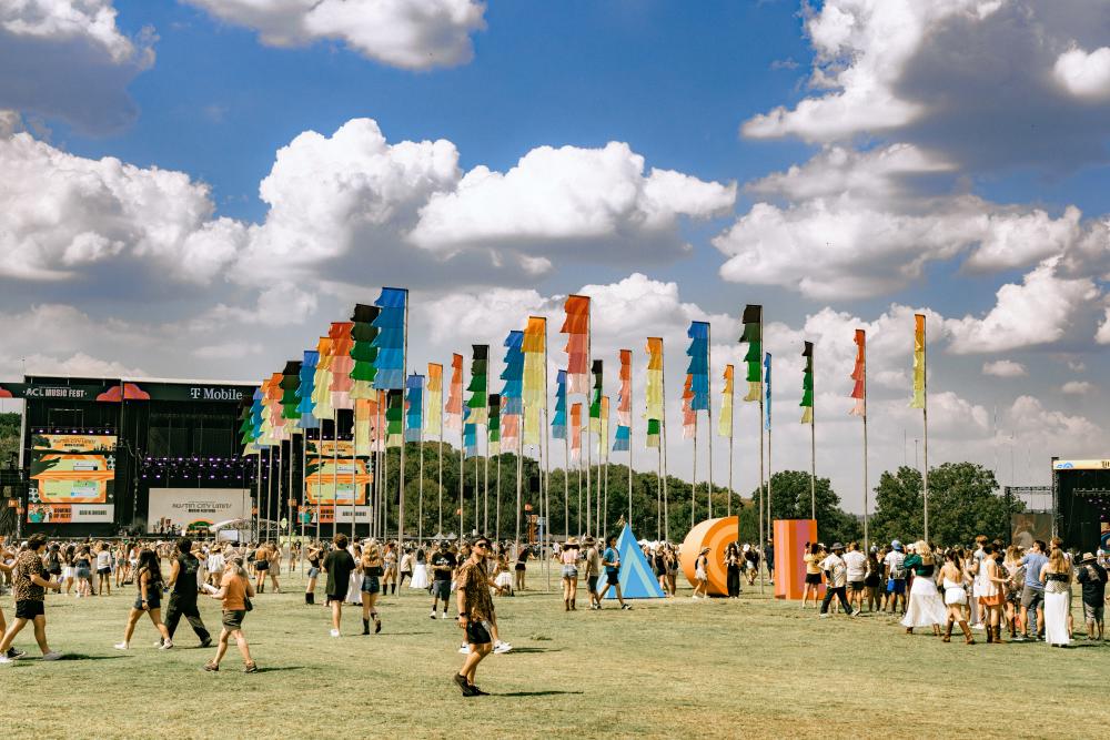 Photo of festival goers walking around in front of the iconic colored flags at ACL Festival.
