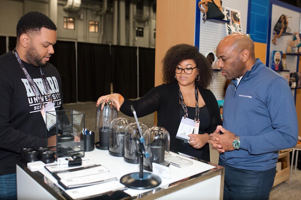 People standing around glass cloches at a conference exhibit.