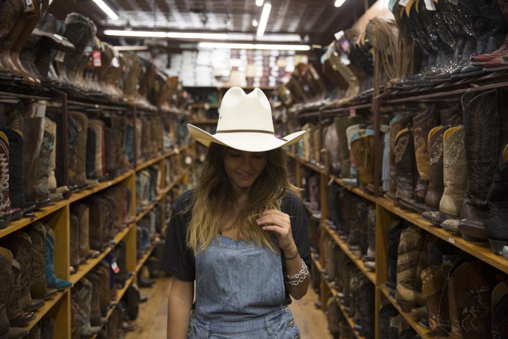 woman wearing cowboy hat in front of rows of boots
