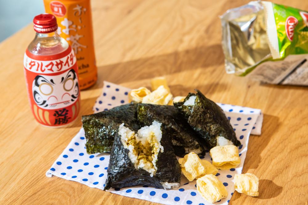 Nori covered hand roll on a blue polka dot paper, next to Asian drinks and snacks.