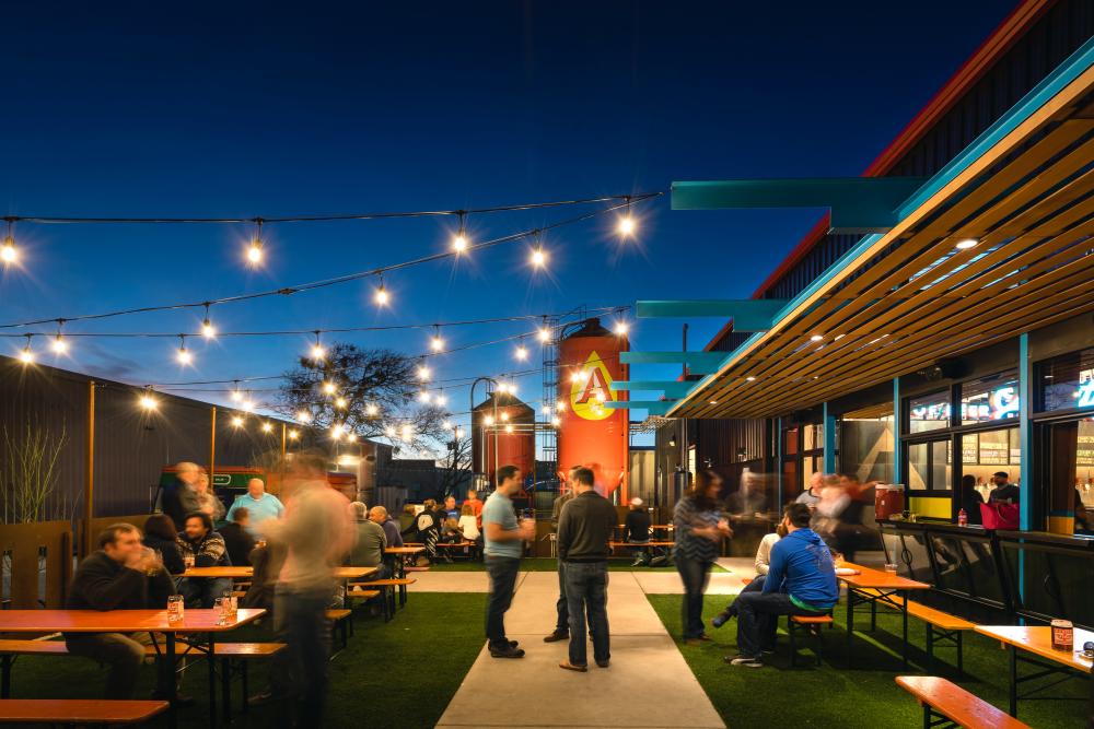 Evening patio at Austin Beerworks with string lights and people standing around the tables