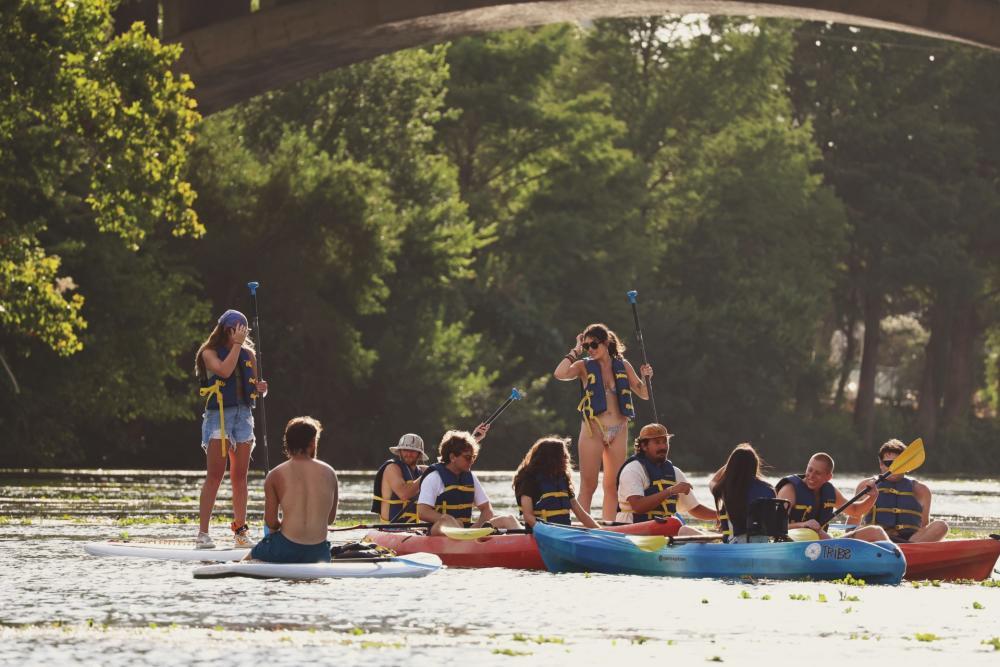 Photo of two girls standing up on paddleboards and some people sitting in kayaks on Lady Bird Lake.