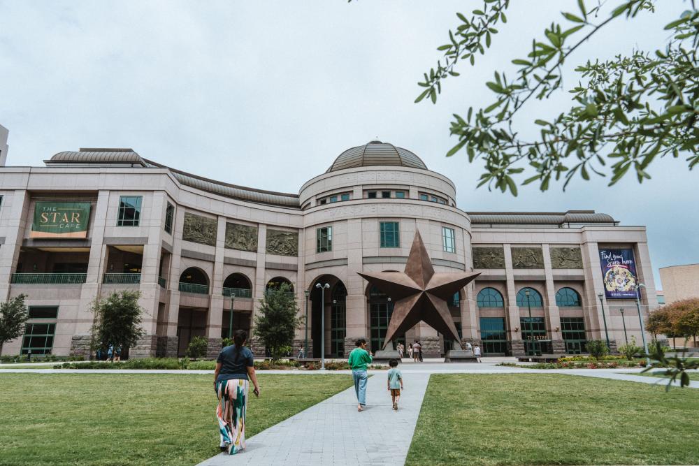 Two children and a woman walking towards the giant star at the entrance of the Bullock Texas State History Museum.
