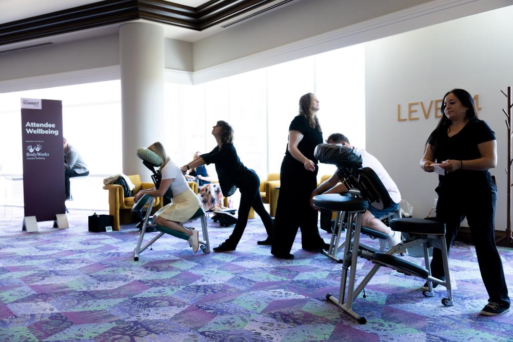 Meeting attendees getting chair massages from massage professionals in a conference wellness lounge.