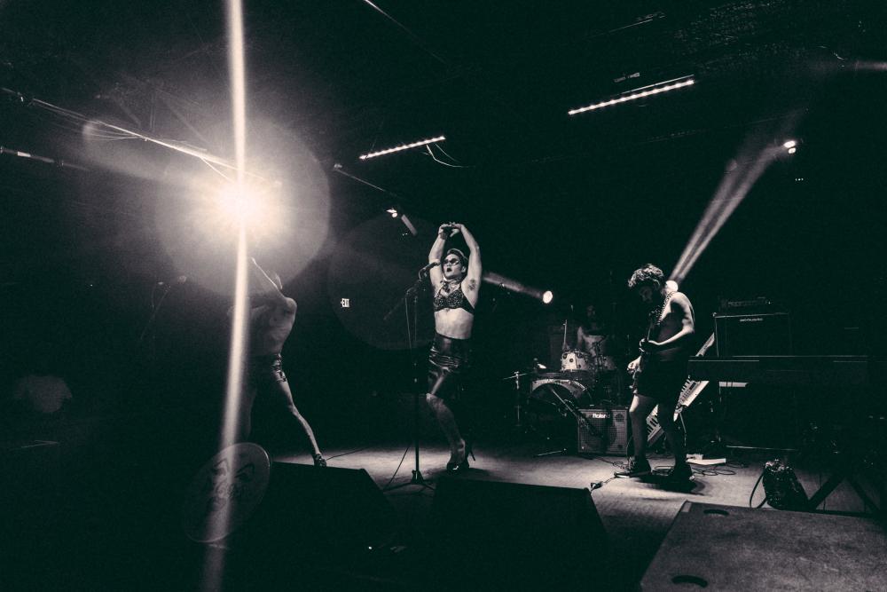 Black and white photo of musician Caleb De Casper in drag performing on stage with band at Empire Control Room