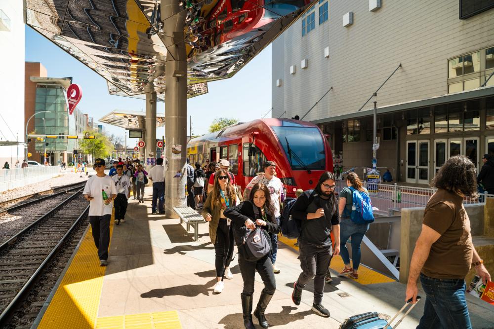 People moving about the CapMetro downtown platform with a red train in the background.
