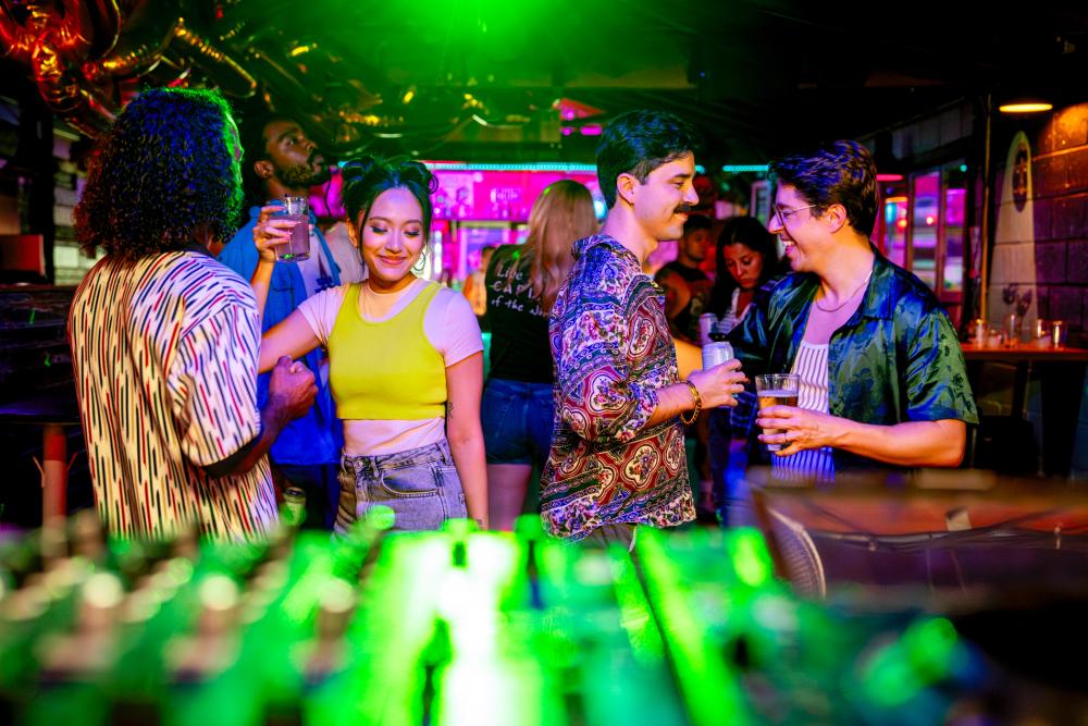 Couples dancing with cocktails in hand in front of a DJ booth with neon lights in an intimate space.