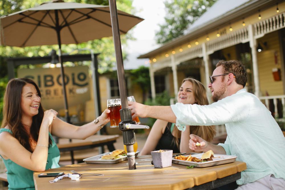 Three poeple cheersing beers on the patio in front of the Cibolo Creek Brewing Co building.