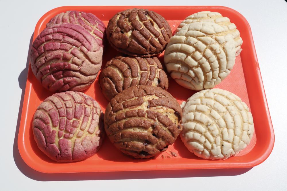 Image of colorful pink, brown and white conchas sitting on a red tray at Comadre Panaderia.