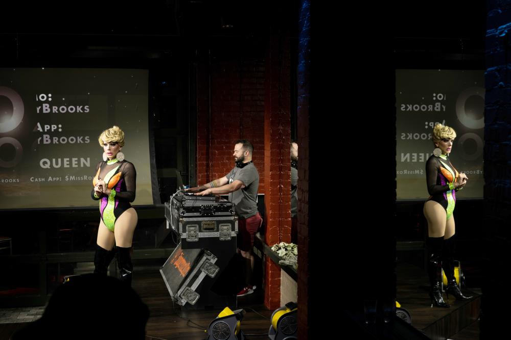 Drag queen performing on stage with DJ behind her.