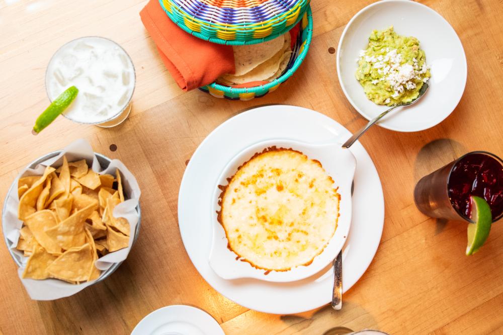 Table of food at El Naranjo including queso, guacamole, a bowl of chips, tortillas and a margarita