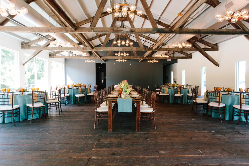 Banquet seating set up in a large white room with dark wood floors and dark wood ceiling beams.